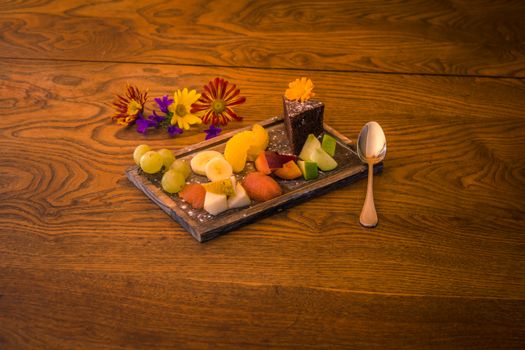 Assiette de fruits variés avec un fondant au chocolat et poire, décorée de fleurs sur une table en bois.