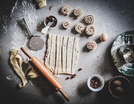 Pâte à brioche étalée avec des rouleaux de pâte, œufs et ingrédients sur un plan de travail en bois.