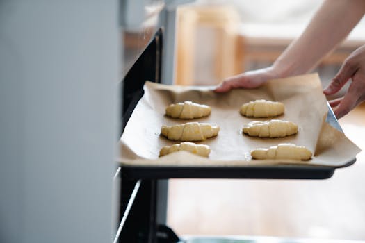 Plaque de cuisson avec des croissants en pâte feuilletée sur du papier sulfurisé, prête à être mise au four.
