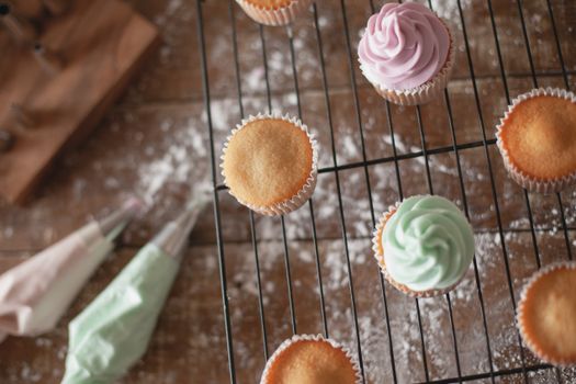 Cupcakes décorés de crème rose et verte sur une grille, avec des ustensiles de pâtisserie en arrière-plan.