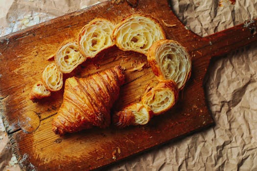 Croissants et pâte feuilletée découpés sur une planche en bois, montrant leur texture feuilletée et dorée.