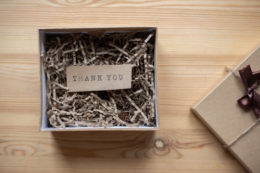 Coffret cadeau en carton avec un message de remerciement sur un lit de papier de soie, posé sur une table en bois.