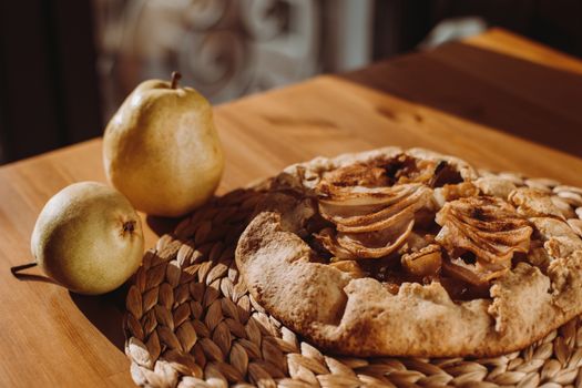 Tarte aux poires et chocolat sur une nappe en osier, entourée de poires fraîches sur une table en bois.