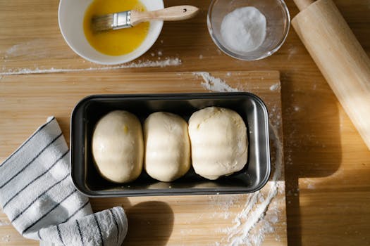 Pâte à brioche moelleuse dans un moule, avec un bol d'œuf battu et un rouleau à pâtisserie en arrière-plan.