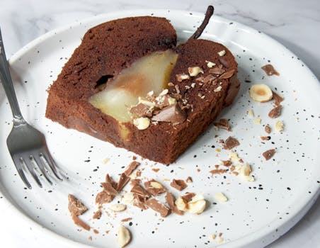 Gâteau fondant au chocolat et poire sur une assiette, décoré de morceaux de chocolat et de noisettes.